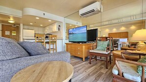 Un espace de vie compact comprenant un canapé, une table basse en bois et un téléviseur posé sur un meuble en bois.