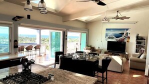 A spacious living area with a kitchen, dining area, and a balcony with a view. - Ocean View Villa with Infinity Pool, Hot Tub & Fire Pit; 5 Min from Beach (Rincón)