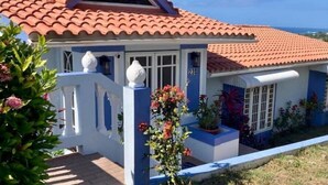 A two-story house with a red-tiled roof, a white porch with decorative vases, and a number '230' on the door. - Ocean View Villa with Infinity Pool, Hot Tub & Fire Pit; 5 Min from Beach (Rincón)
