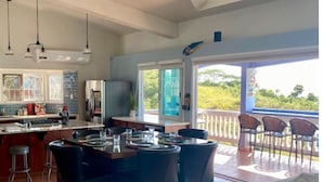 A spacious kitchen with a central island, a dining area with chairs, and a large sliding glass door leading to an outdoor patio. - Ocean View Villa with Infinity Pool, Hot Tub & Fire Pit; 5 Min from Beach (Rincón)