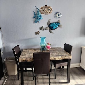 A dining area with a marble table, four chairs, a blue vase, and decorative wall art including a fish and a turtle.