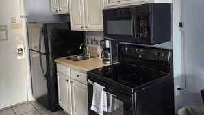 Une cuisine compacte équipée d’un réfrigérateur, d’un four à micro-ondes, d’une cuisinière et d’une machine à café posée sur le plan de travail.