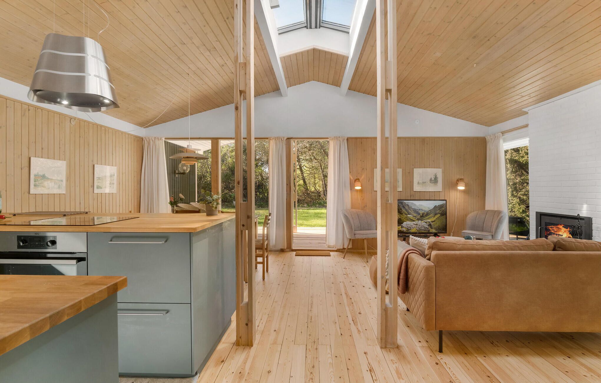 Une cuisine moderne avec un plan de travail en bois et une cuisinière intégrée, un salon confortable avec un canapé et une cheminée, et une grande fenêtre donnant sur un jardin.