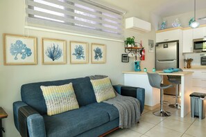 A living room with a sofa, a small kitchen area, and framed artwork on the wall.