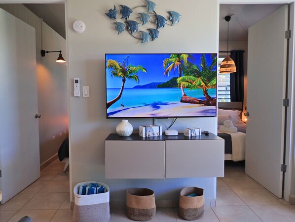 A modern living room with a flat-screen TV mounted on a white cabinet, a decorative wall art of fish, and a view of a beach scene on the TV screen.