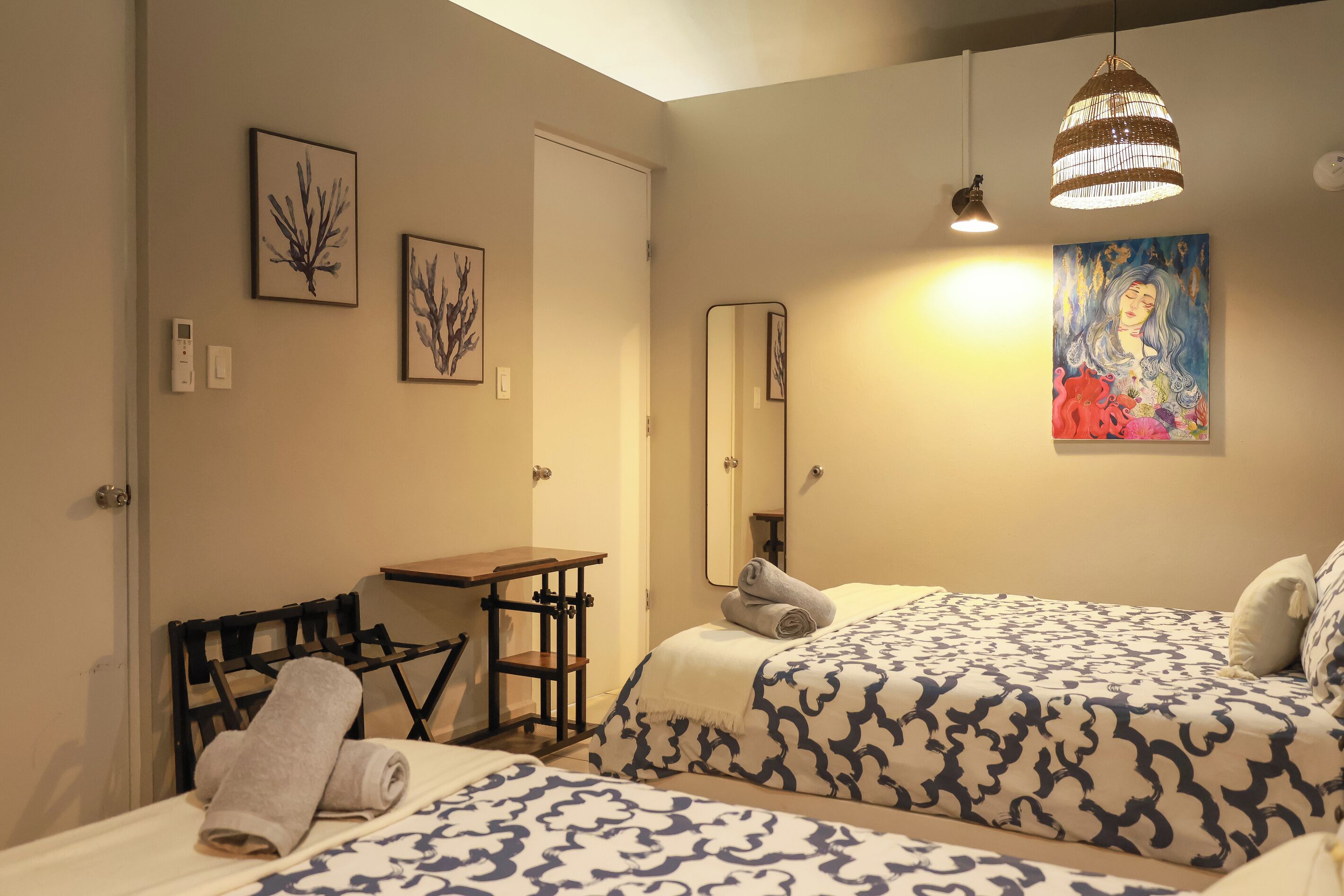A hotel room with two beds, a desk, a chair, a mirror, and artwork on the walls.