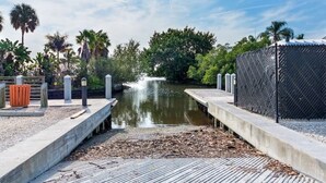 Een betonnen steiger die uitkomt bij een kalm waterlichaam met een kleine waterval, omgeven door weelderige begroeiing en een metalen hek.