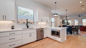 A modern kitchen with white cabinetry, a built-in dishwasher, and a central island with a microwave. - Charming Luxury Home near Heights & close to Downtown-The Houston oasis . (Houston)