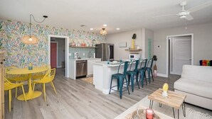 A modern kitchen with white cabinets, a central island, and teal chairs. - Colorful home with game area (Bradenton)