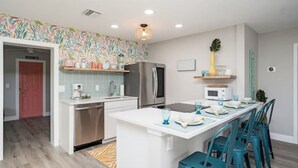 A modern kitchen with white countertops, a stainless steel refrigerator, and a central island with bar stools. - Colorful home with game area (Bradenton)