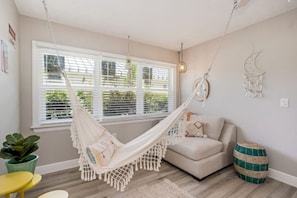 A room with a hammock, a sofa, a round table, and a potted plant.