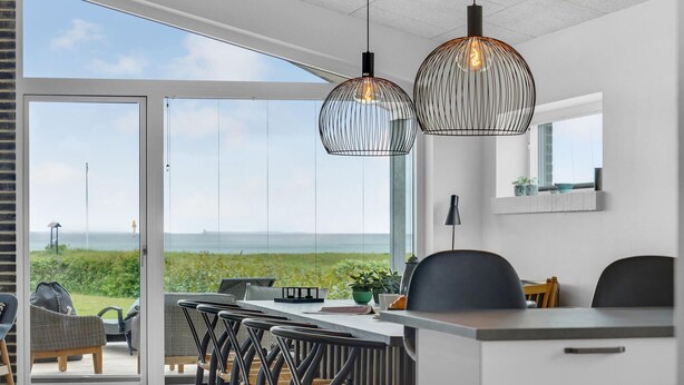 Un espace de salle à manger moderne avec vue sur la mer, comprenant une table avec des chaises et des luminaires suspendus.