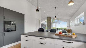Une cuisine moderne dotée d’un four encastré, d’un coin repas agrémenté d’un mur en briques apparentes et d’une grande fenêtre offrant une vue sur la verdure.