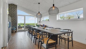 Un vaste espace dédié à la salle à manger, avec une longue table et des chaises, un mur en briques et de grandes fenêtres offrant une vue sur l’extérieur.