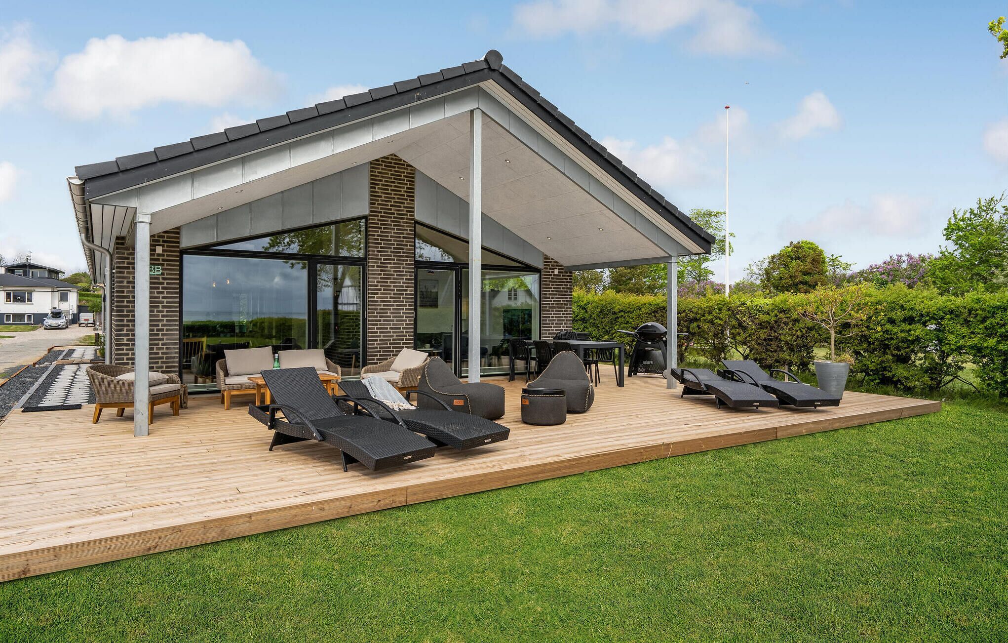 Um pátio moderno ao ar livre com cadeiras de lounge, uma mesa e área de churrasco.