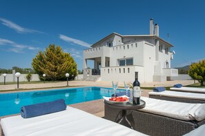 Un espace aménagé au bord de la piscine, avec des chaises longues, une table sur laquelle se trouvent une bouteille et des verres, et un bâtiment blanc en arrière-plan.