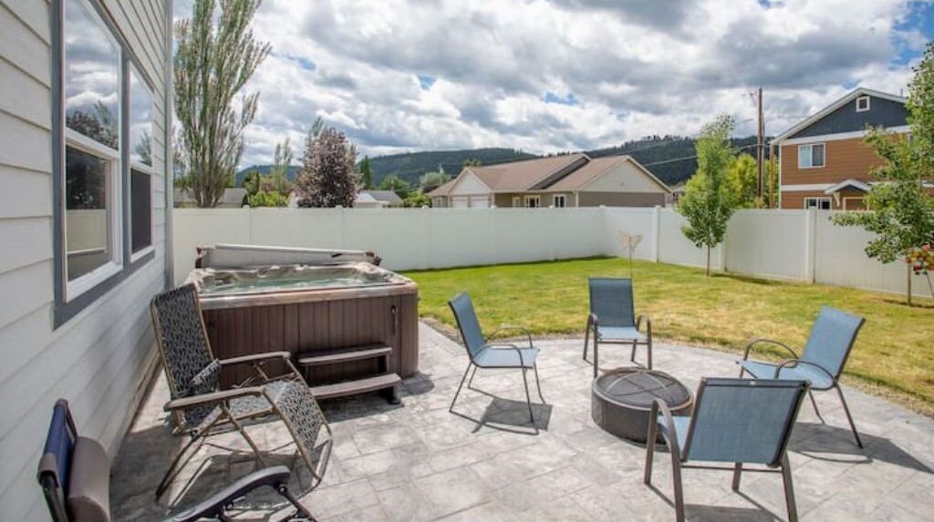 Une terrasse à l’arrière de la maison, avec un jacuzzi, du mobilier d’extérieur et une vue sur les maisons voisines.