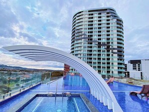 A modern hotel with a curved swimming pool and a view of a tall building in the background. - Spacious 1 Bed Apartment, parking, gym, pool (Gungahlin)