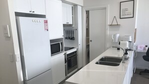 A modern kitchen with white cabinetry, a built-in microwave, a sink, and a coffee maker. - Spacious 1 Bed Apartment, parking, gym, pool (Gungahlin)