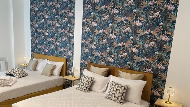 Una habitación de hotel con dos camas, papel tapiz floral y lámparas de noche.