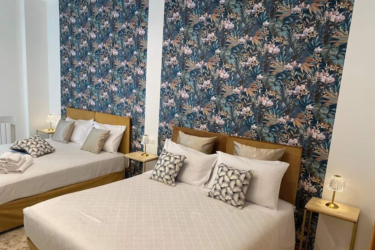 Quarto de hotel com duas camas, papel de parede floral e abajures.