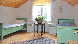 A small, cozy room with two single beds, a small table with a plant, a window with curtains, and a wooden ceiling.