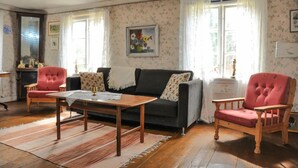 A cozy living room with a dark sofa, two red armchairs, a wooden coffee table, and a patterned rug.