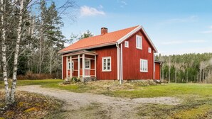 A red wooden house with a sloped roof, a porch, and a visible chimney.