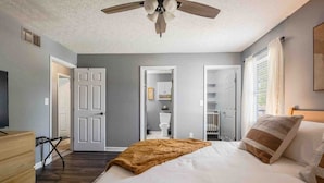 Un dormitorio con cama, ventilador de techo, armario y puerta que da a un baño.