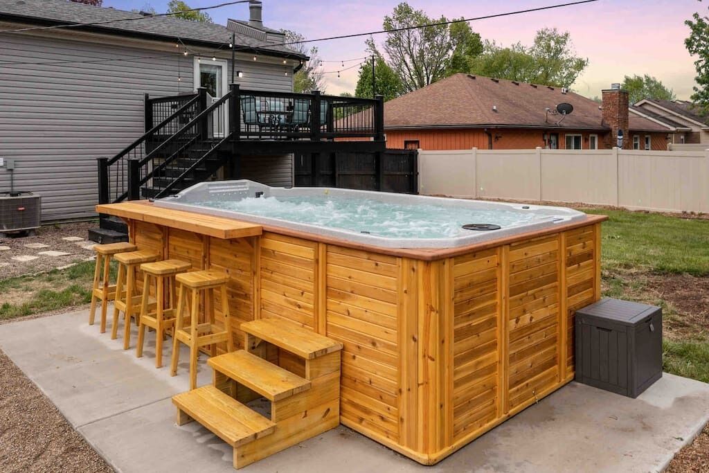 Un bain à remous en bois doté de sièges et de marches intégrés, entouré d’une terrasse en béton.