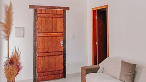A living room with a wooden door, a sofa, a coffee table, and a vase with dried plants. - Suítes D'Ajuda Inn (Porto Seguro)