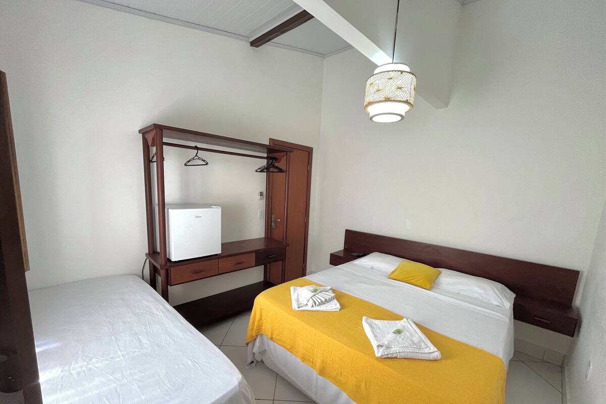 Une chambre d’hôtel comprenant un lit, un petit bureau avec un réfrigérateur, une armoire et un luminaire suspendu.