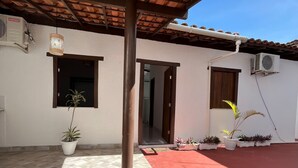A covered outdoor area with a tiled floor, potted plants, and a red carpet. - Suítes D'Ajuda Inn (Porto Seguro)