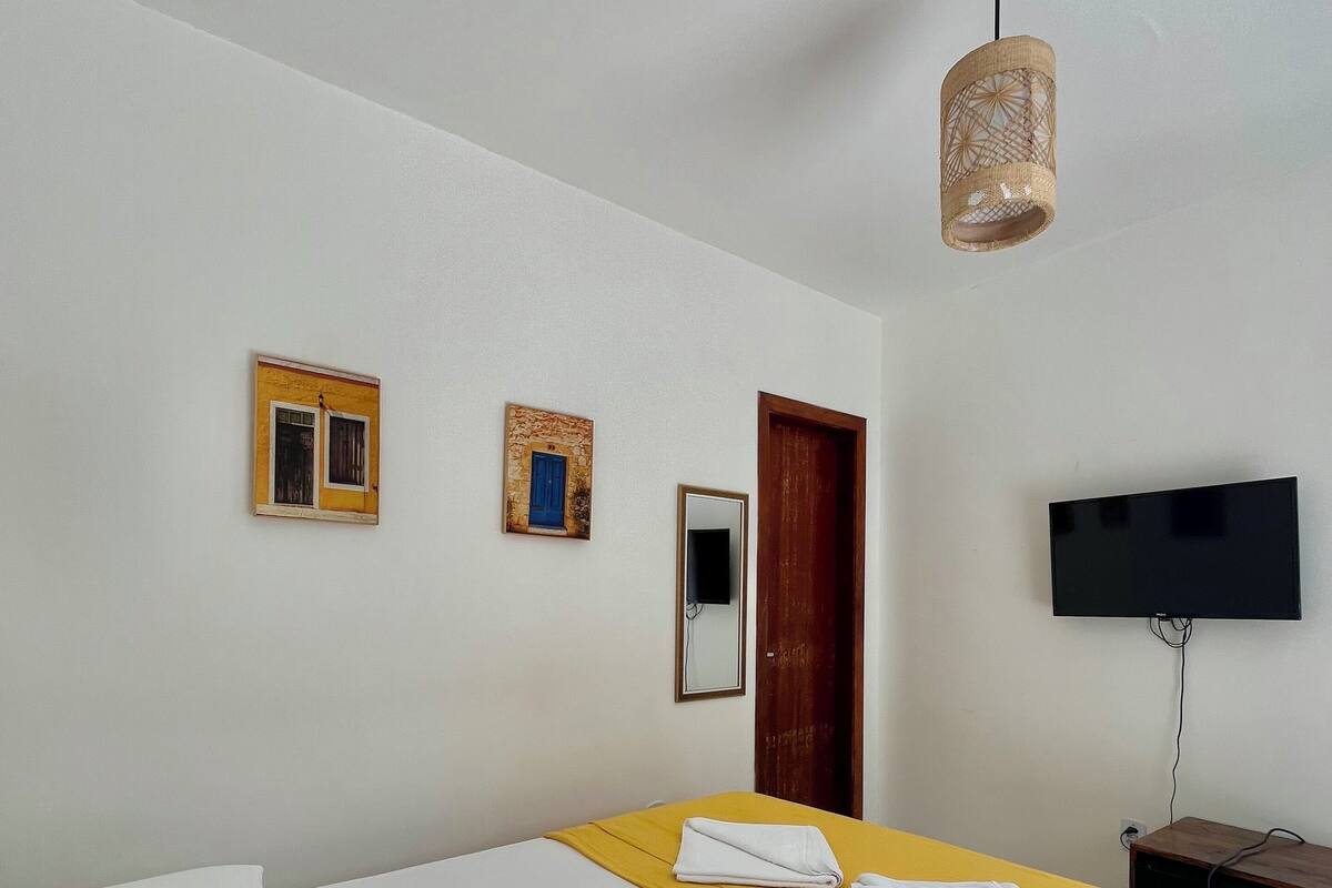 Une chambre d’hôtel avec un lit, un oreiller jaune, une télévision et un luminaire fixé au mur.