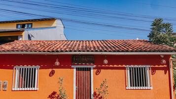 Um edifício vermelho com telhado ladrilhado, duas plantas em vasos na frente e uma placa sobre a porta.