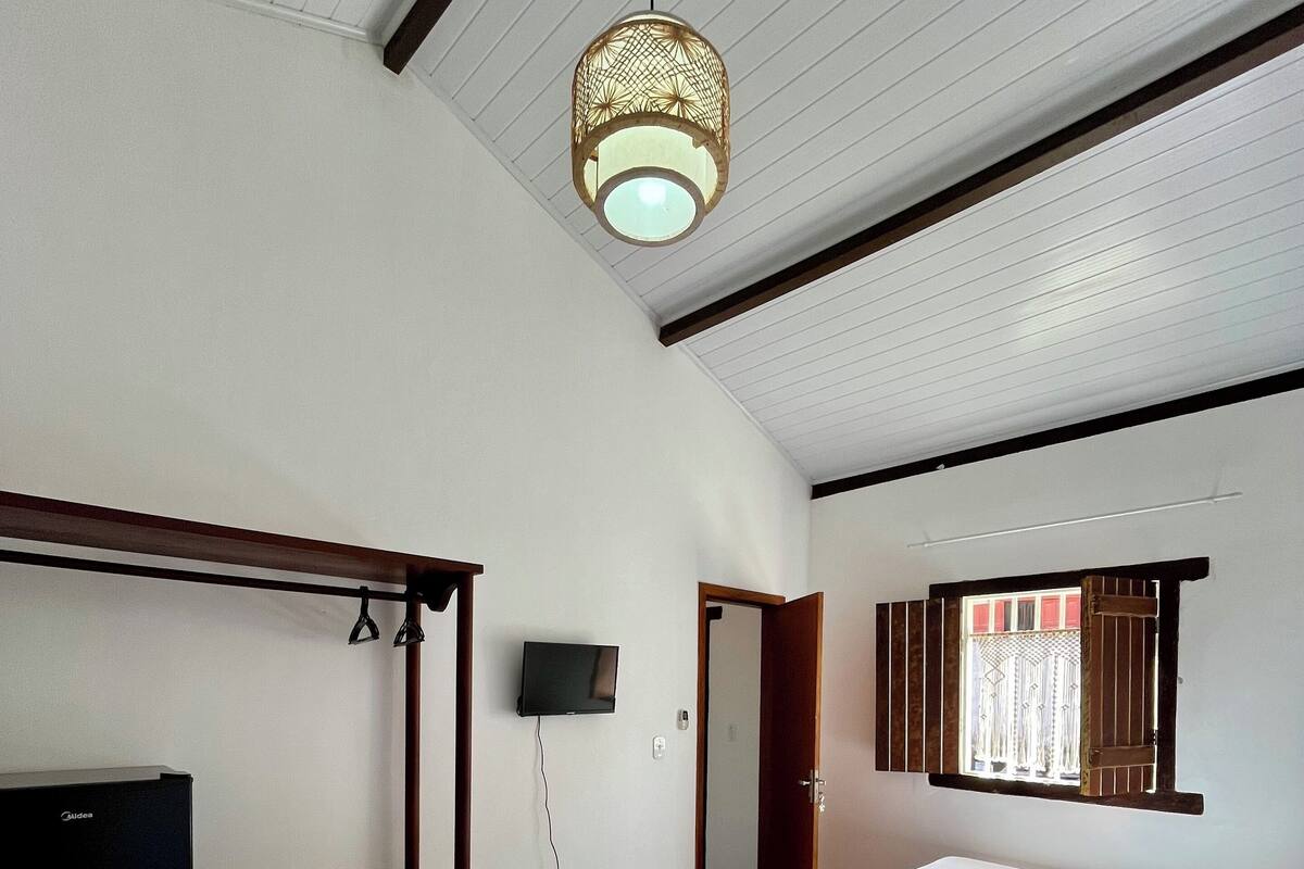 Une chambre d’hôtel comprenant un lit, un bureau avec une télévision, un luminaire au plafond et une fenêtre avec des rideaux.