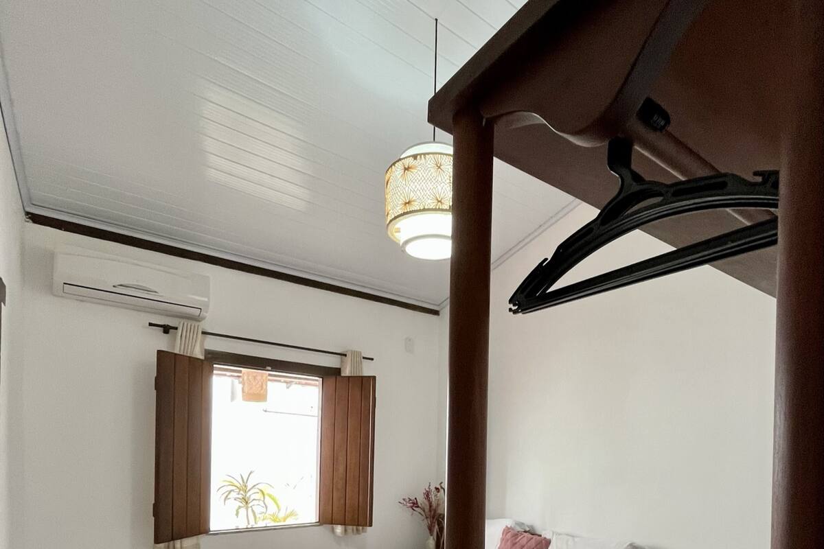 Une chambre à coucher avec un lit, une fenêtre avec des rideaux, un luminaire suspendu et une tête de lit en bois.