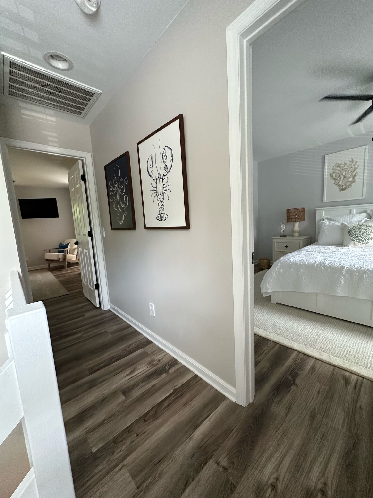 Un dormitorio con una cama, una mesita de noche y una lámpara de pared. Hay un pasillo que conduce a otra habitación.