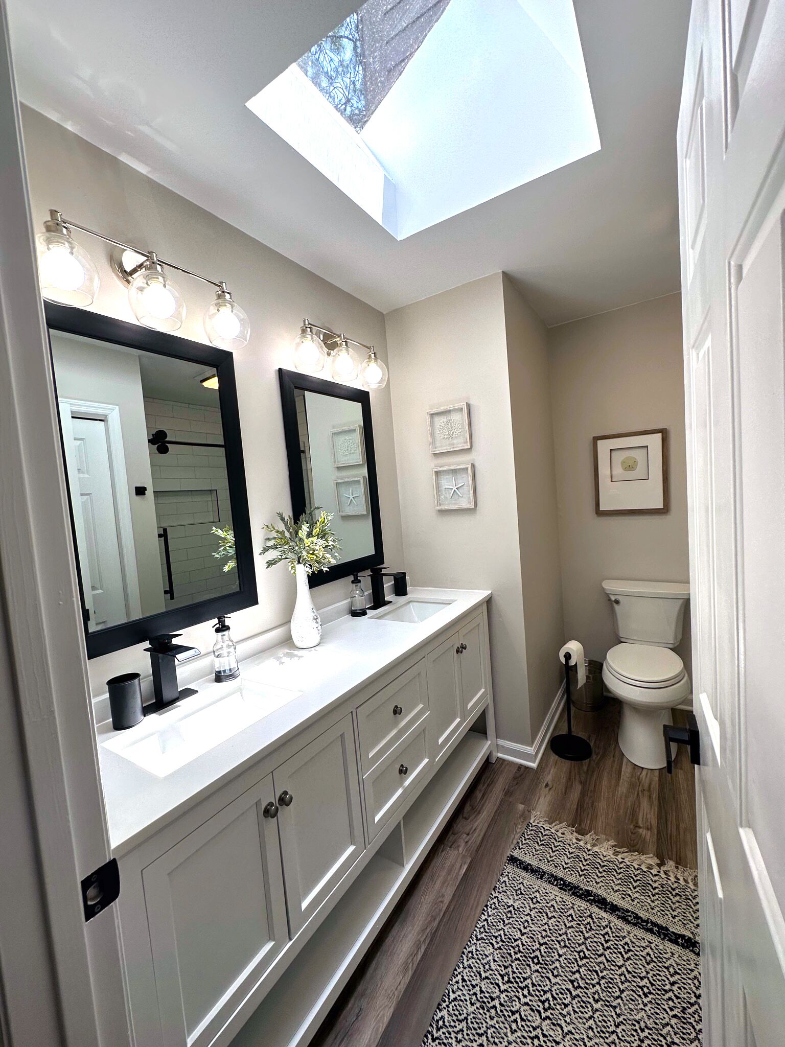 A bathroom with a skylight, a large mirror, a white sink, and a toilet.