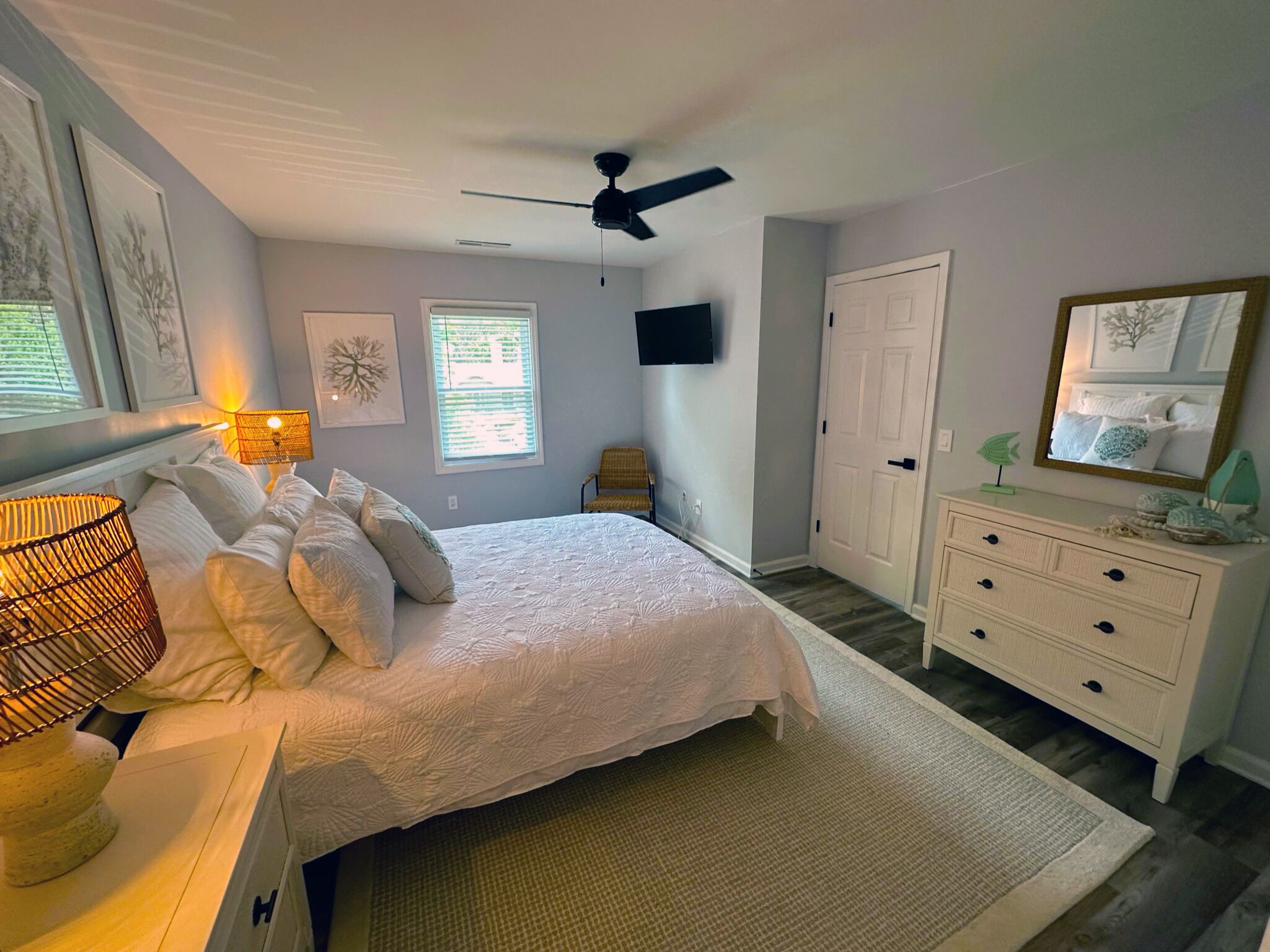 Un dormitorio con cama, lámparas de noche, cómoda, espejo y ventilador de techo.