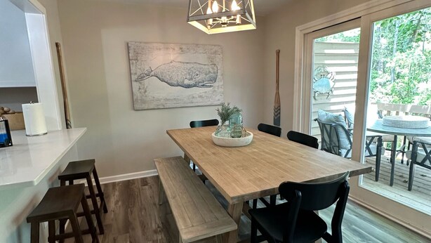 Un coin repas avec une table en bois, des bancs et des chaises noires. Un luminaire est suspendu au-dessus de la table.