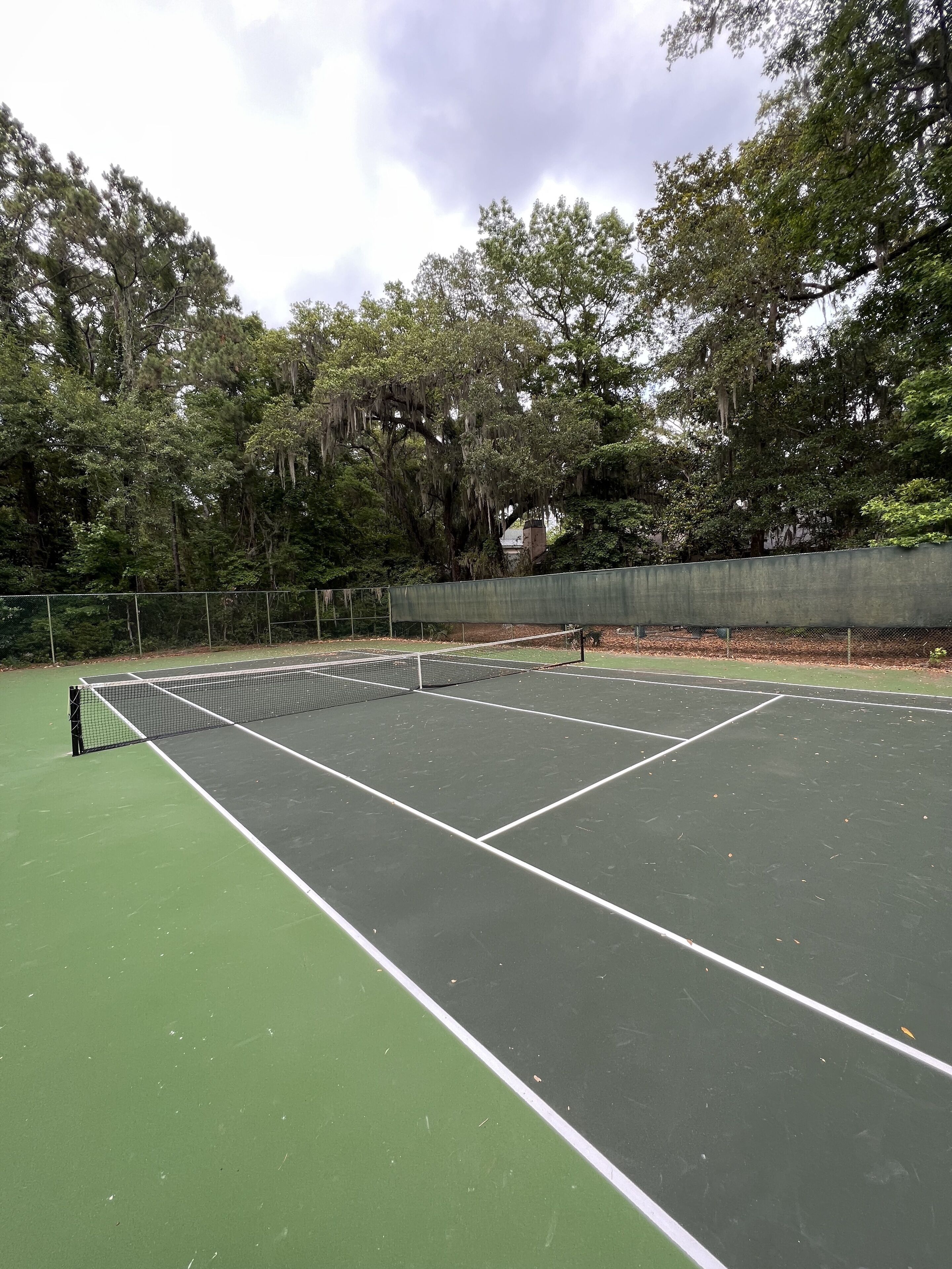 A tennis court with a net, surrounded by trees and a fence.