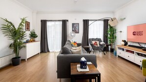 A modern living room with a grey sofa, a small table with a tissue box, a TV displaying "GUEST READY", and a large potted plant. - GuestReady - Trendy stay near Brick Lane Market (London)