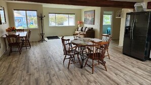 Un salon spacieux doté d’un plancher en bois, un coin repas avec des chaises en bois, un canapé et un réfrigérateur noir.