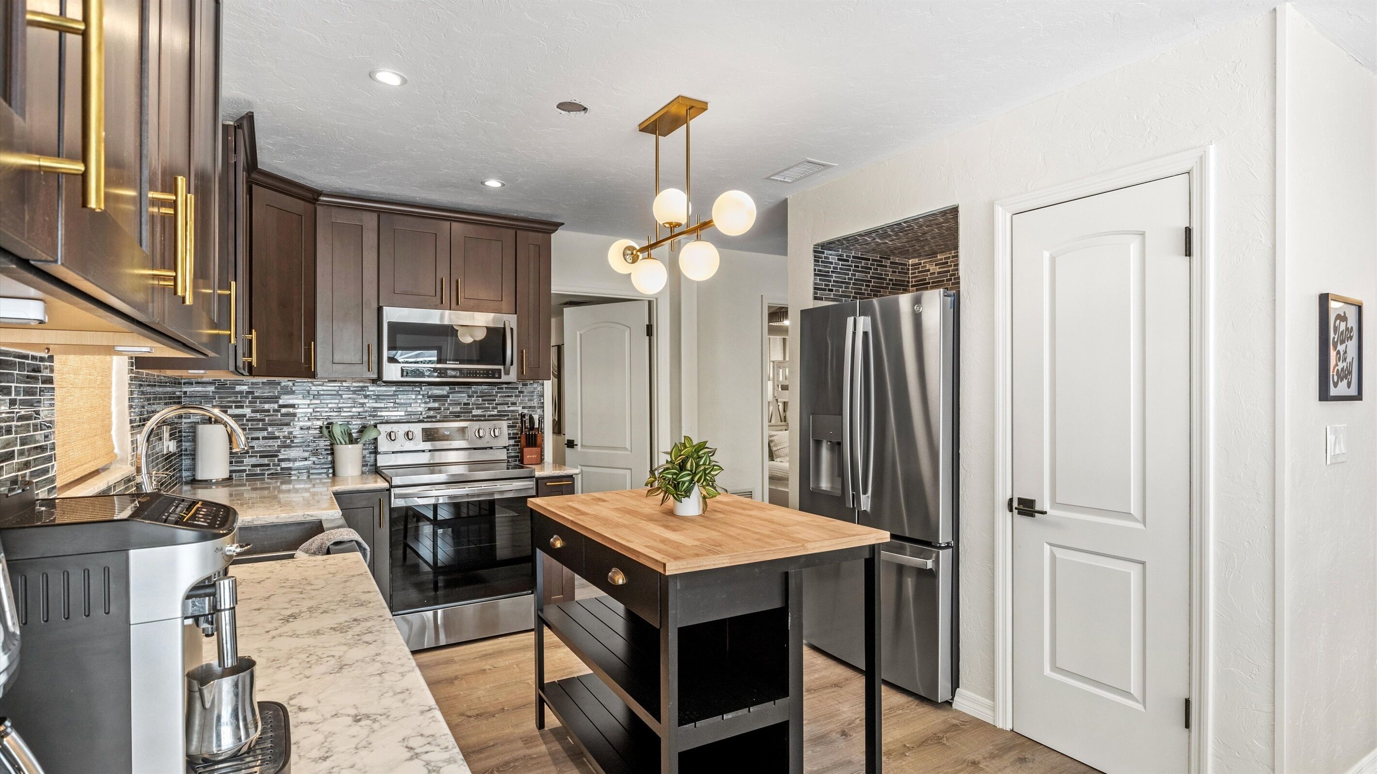 A modern kitchen with stainless steel appliances, a wooden island, and a black countertop.