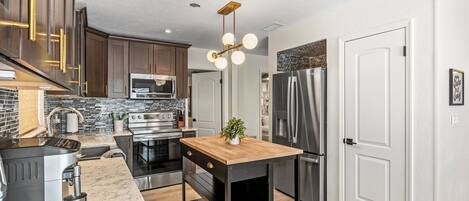 A modern kitchen with stainless steel appliances, a wooden island, and a black countertop.