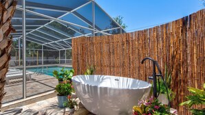 Un espace piscine extérieur moderne, doté d’une structure fermée par des parois de verre, d’une clôture en bambou et d’une baignoire sur pied.