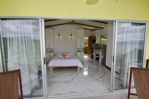 A bedroom with a bed, a wooden bench, and a sliding glass door leading to a kitchen.