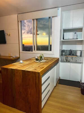 Una cocina moderna con una isla de madera, armarios blancos y vistas a un atardecer a través de un ventanal grande.