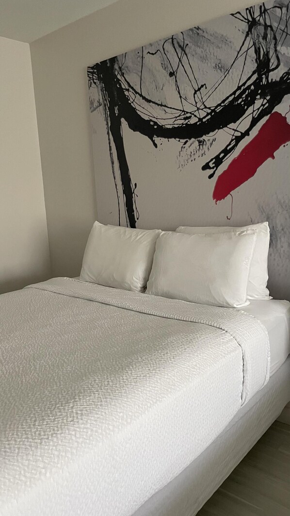 Relax in a serene bedroom with a large bed, minimalist decor, and a striking piece of abstract art.